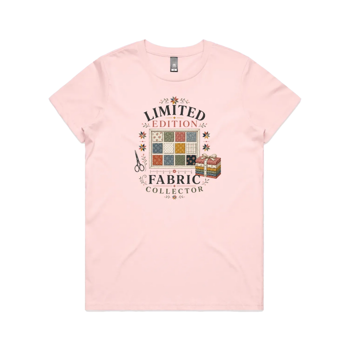 A pale pink short-sleeve crewneck t-shirt featuring the text 'Limited Edition Fabric Collector' surround a fabric swatch board, a tied bundle of fabric and scissors.