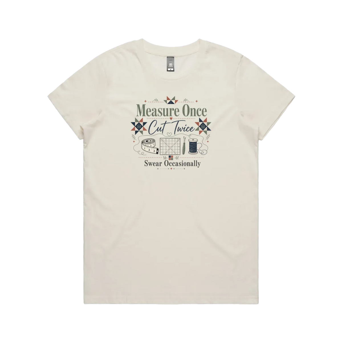 A pale cream short-sleeve crewneck t-shirt with the graphic 'Measure Once, Cut Twice, Swear Occasionally'. The design includes patchwork stars and quilting accessories.