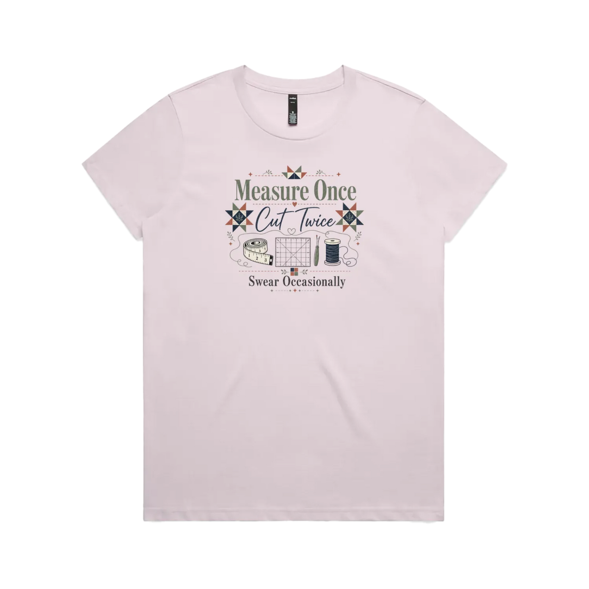 A pale mauve short-sleeve crewneck t-shirt with the graphic 'Measure Once, Cut Twice, Swear Occasionally'. The design includes patchwork stars and quilting accessories.