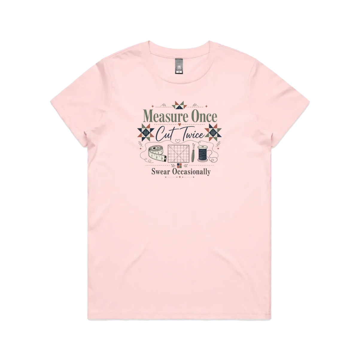A pale pink short-sleeve crewneck t-shirt with the graphic 'Measure Once, Cut Twice, Swear Occasionally'. The design includes patchwork stars and quilting accessories.