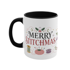 The left side of a white ceramic mug with a black handle and interior, decorated with a bobbin, thread spool,  pincushion and holly and the text ‘Merry Stitchmas’.