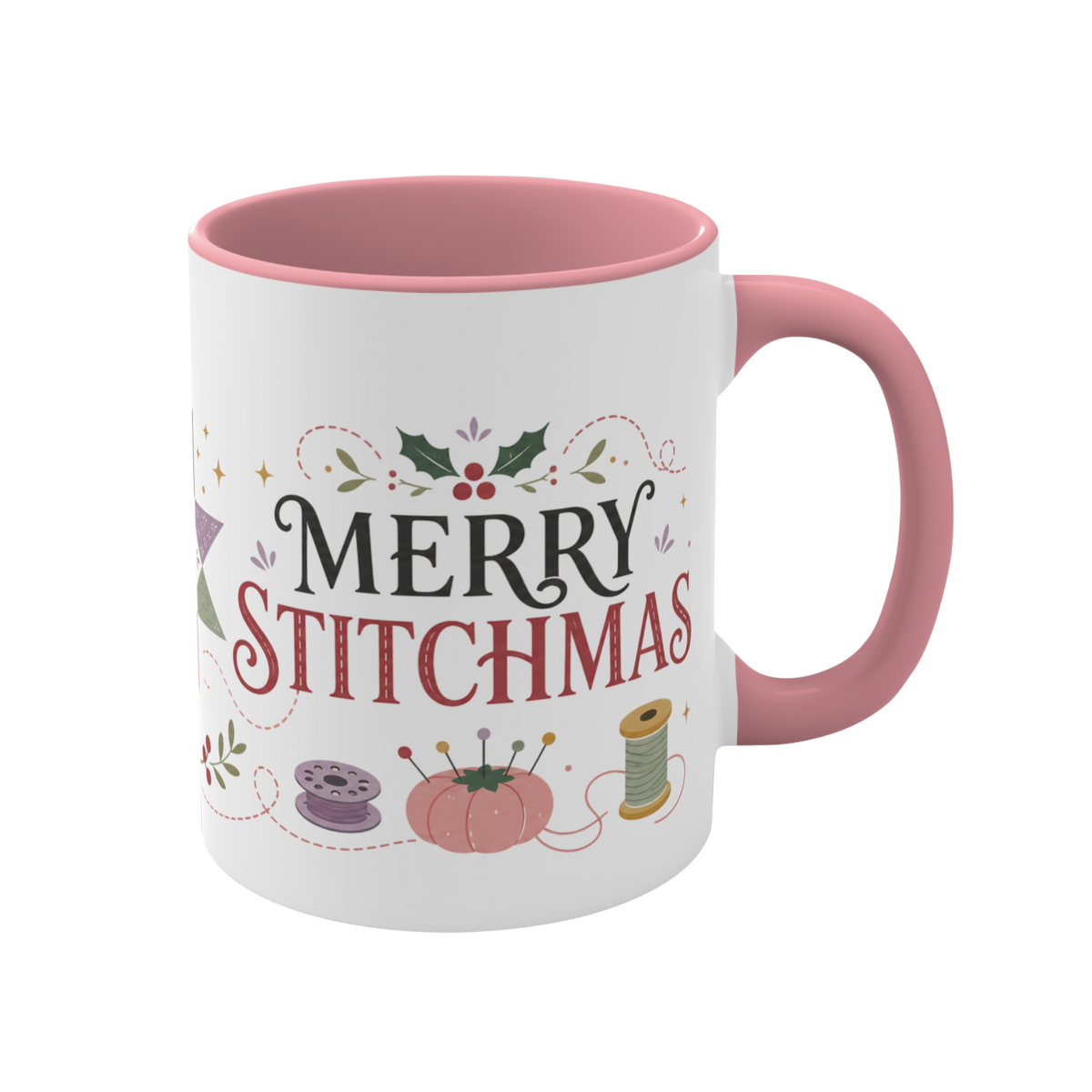The right side of a white ceramic mug with a pink handle and interior, decorated with a bobbin, thread spool,  pincushion and holly and the text ‘Merry Stitchmas’.