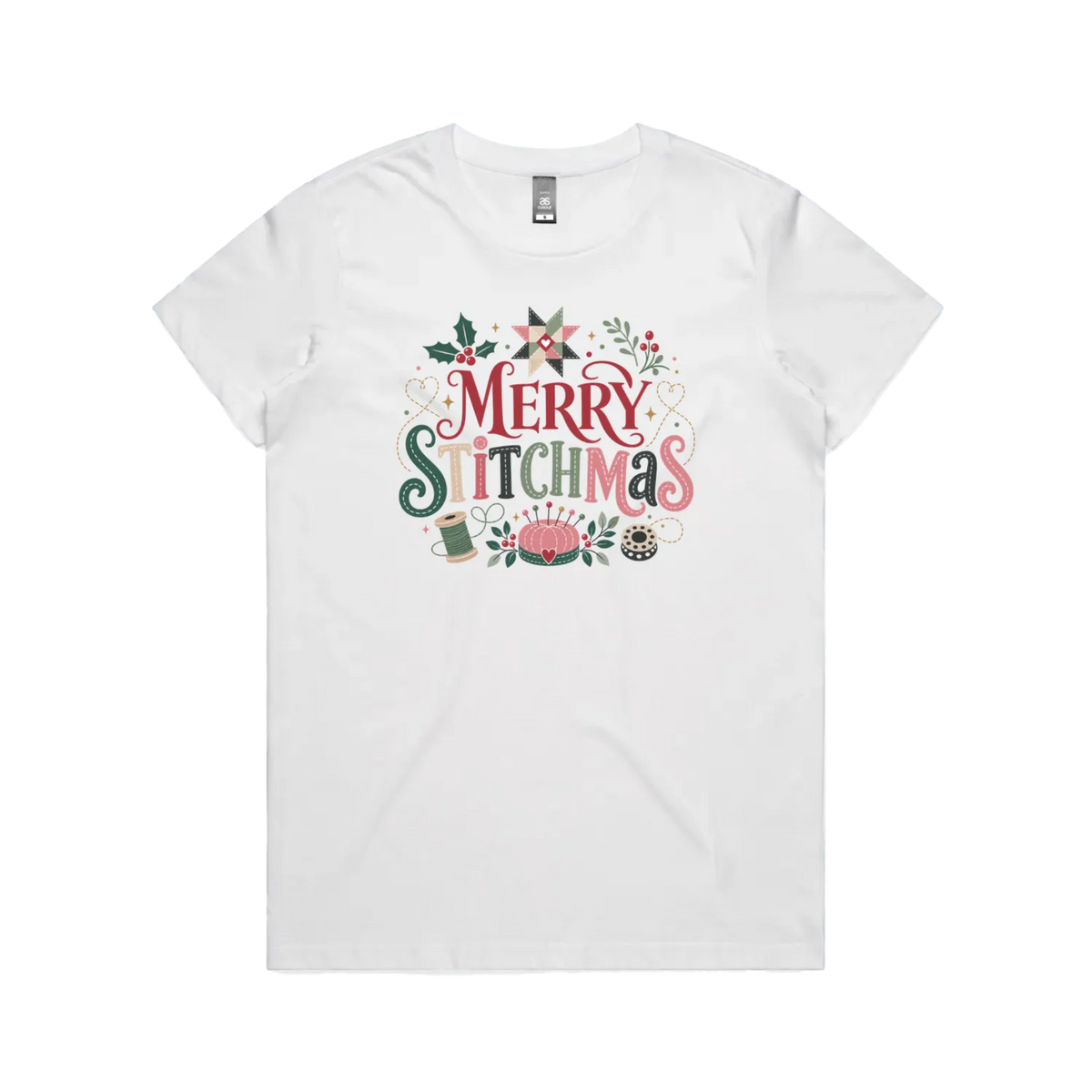 A white short-sleeve crewneck t-shirt featuring a colorful graphic print on the front that reads 'Merry Stitchmas' in decorative lettering with Christmas and quilting-themed illustrations.