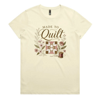 A very pale yellow short-sleeve crewneck t-shirt featuring a vintage-style quilt graphic with the text 'Made To Quilt' in brown script and floral illustrations.