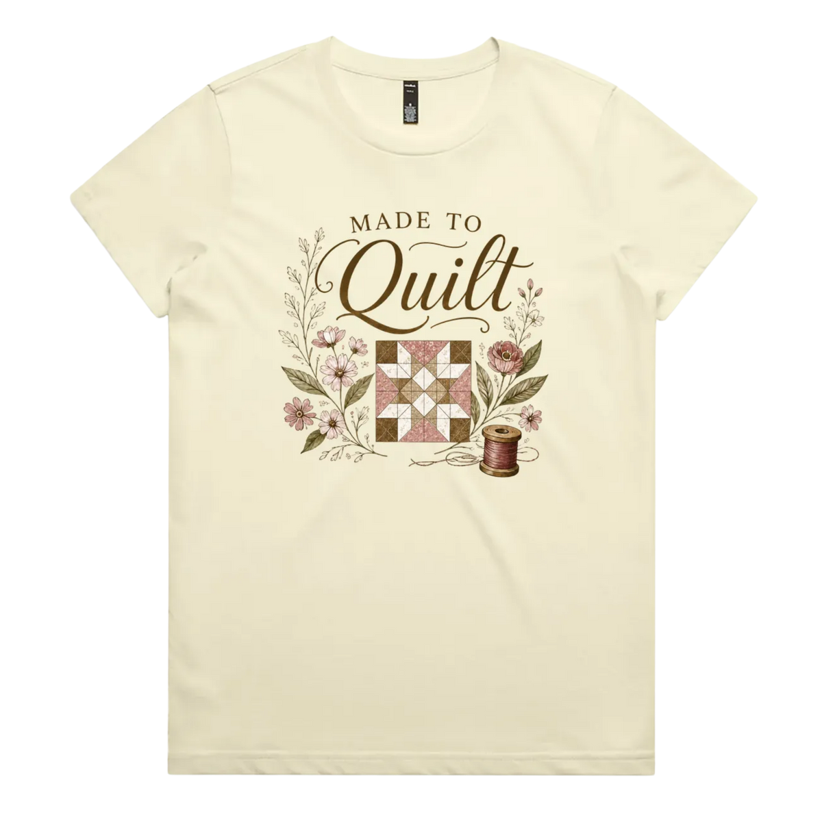 A very pale yellow short-sleeve crewneck t-shirt featuring a vintage-style quilt graphic with the text 'Made To Quilt' in brown script and floral illustrations.