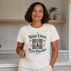 A woman wearing a cream-colored graphic t-shirt with the text 'Nine Lives Nine Patches' and a colorful patchwork design, holding a white mug in a bright kitchen setting.