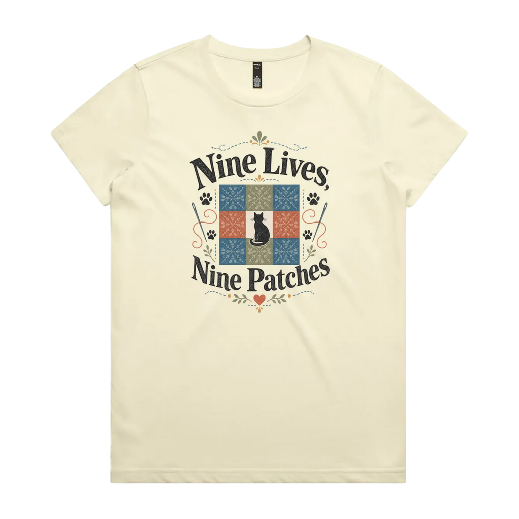 A light butter yellow short-sleeve t-shirt with a colorful graphic on the front that reads 'Nine Lives, Nine Patches' around a nine patch quilt block with a black cat silhouette in the middle.