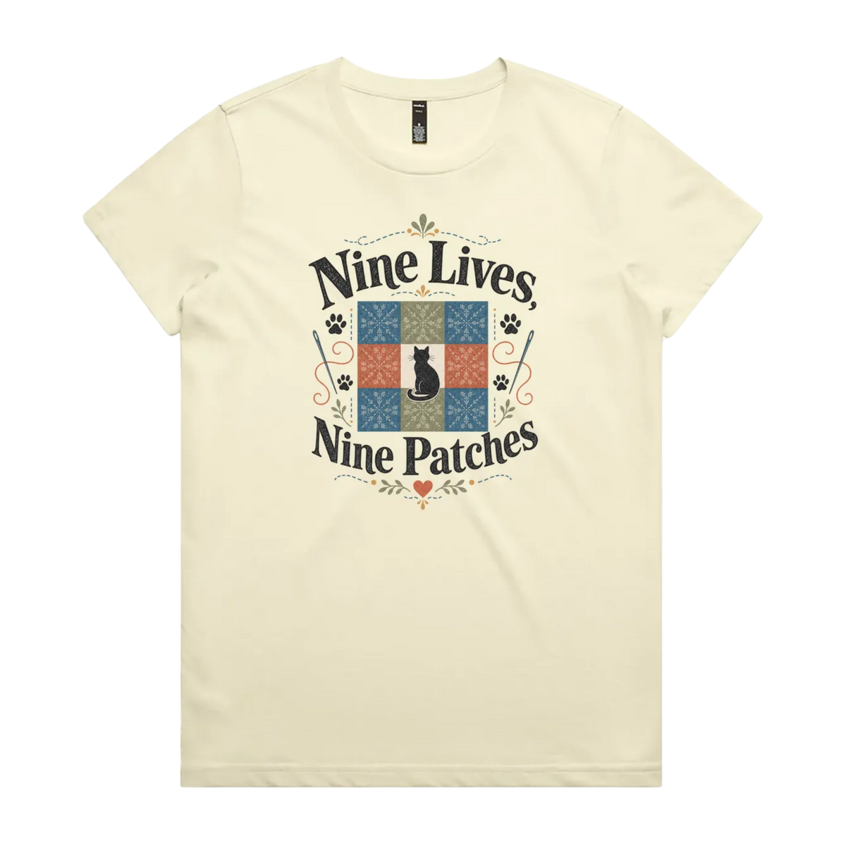 A light butter yellow short-sleeve t-shirt with a colorful graphic on the front that reads 'Nine Lives, Nine Patches' around a nine patch quilt block with a black cat silhouette in the middle.
