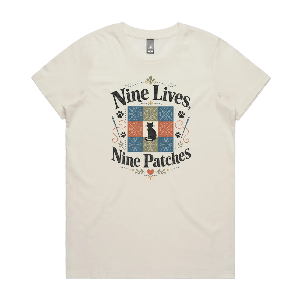 A light cream short-sleeve t-shirt with a colorful graphic on the front that reads 'Nine Lives, Nine Patches' around a nine patch quilt block with a black cat silhouette in the middle.
