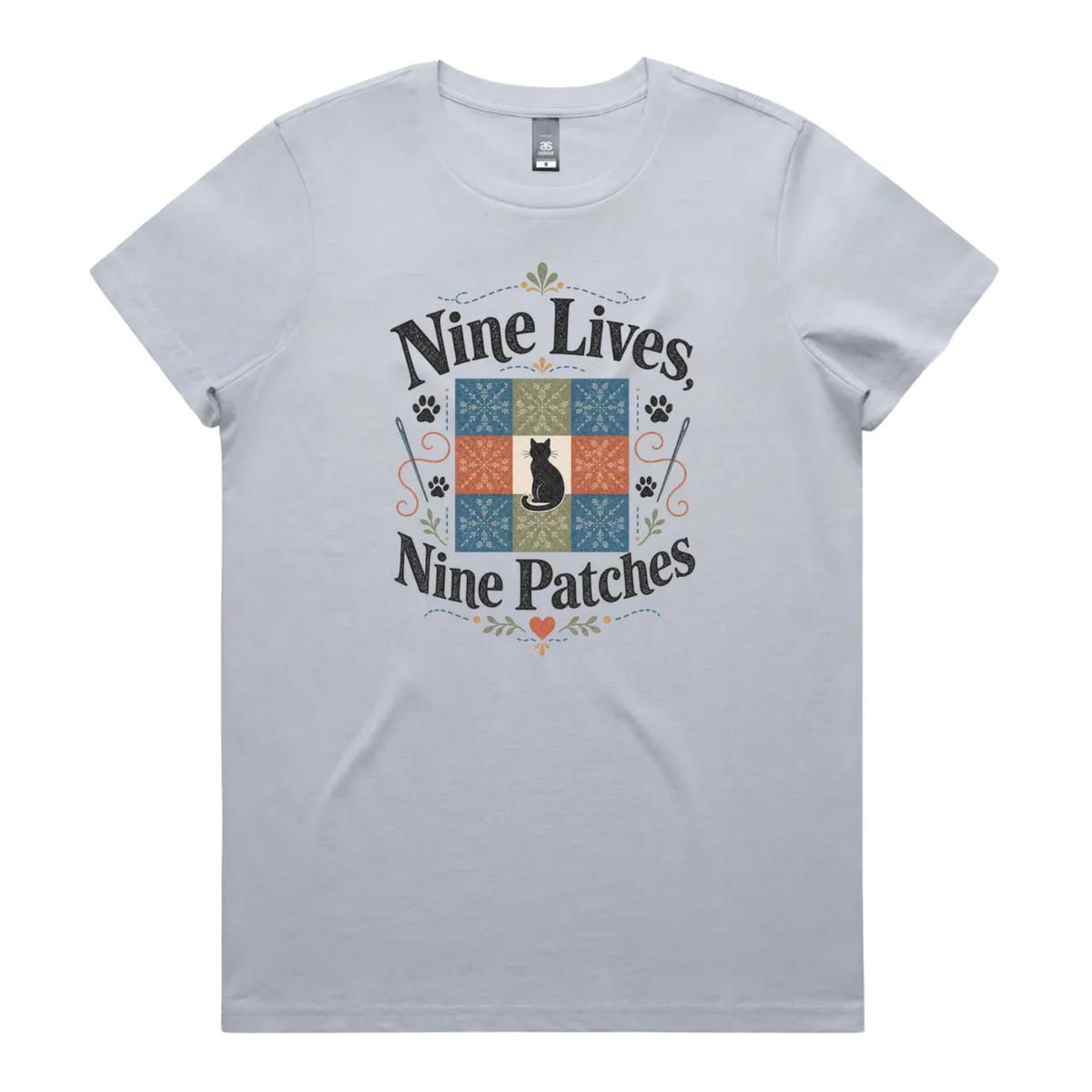A light powder blue short-sleeve t-shirt with a colorful graphic on the front that reads 'Nine Lives, Nine Patches' around a nine patch quilt block with a black cat silhouette in the middle.