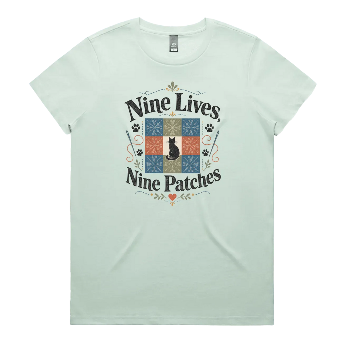 A light seafoam green short-sleeve t-shirt with a colorful graphic on the front that reads 'Nine Lives, Nine Patches' around a nine patch quilt block with a black cat silhouette in the middle.