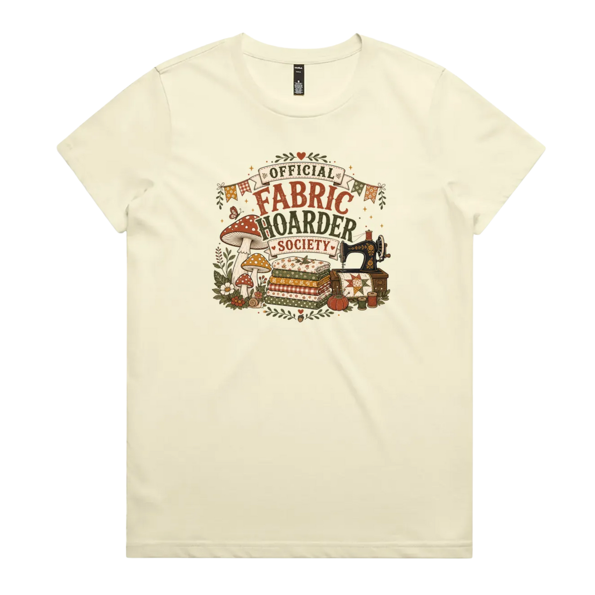 A pale butter yellow crewneck short-sleeved t-shirt with the words 'Official Fabric Hoarder Society' above an illustration of a stack of fabric, a sewing machine and a group of muchrooms, flowers and a snail.