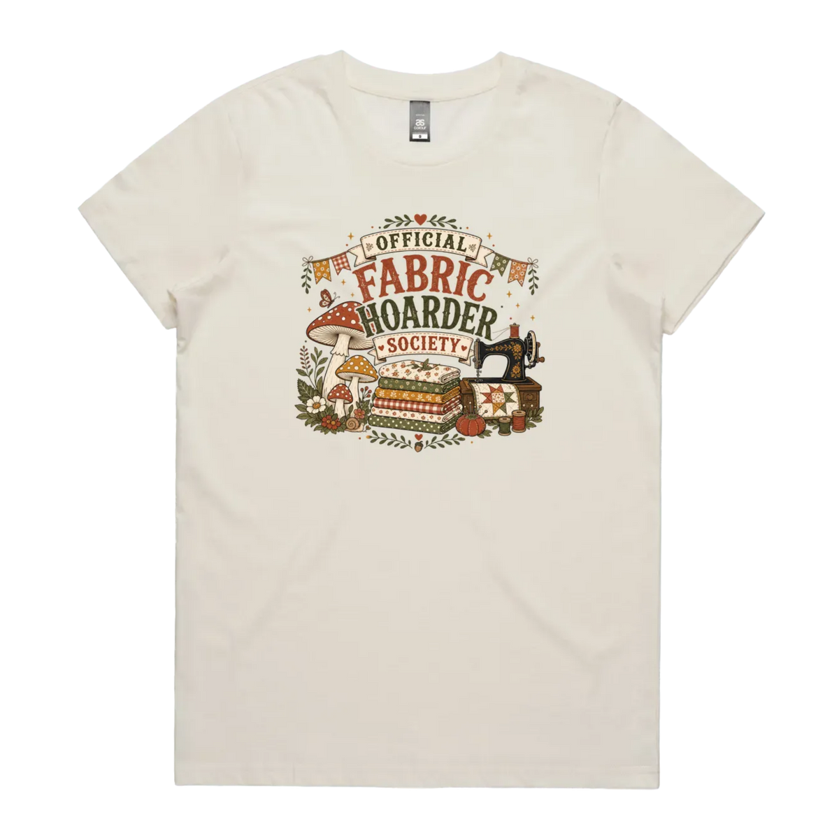 A pale cream crewneck short-sleeved t-shirt with the words 'Official Fabric Hoarder Society' above an illustration of a stack of fabric, a sewing machine and a group of muchrooms, flowers and a snail.
