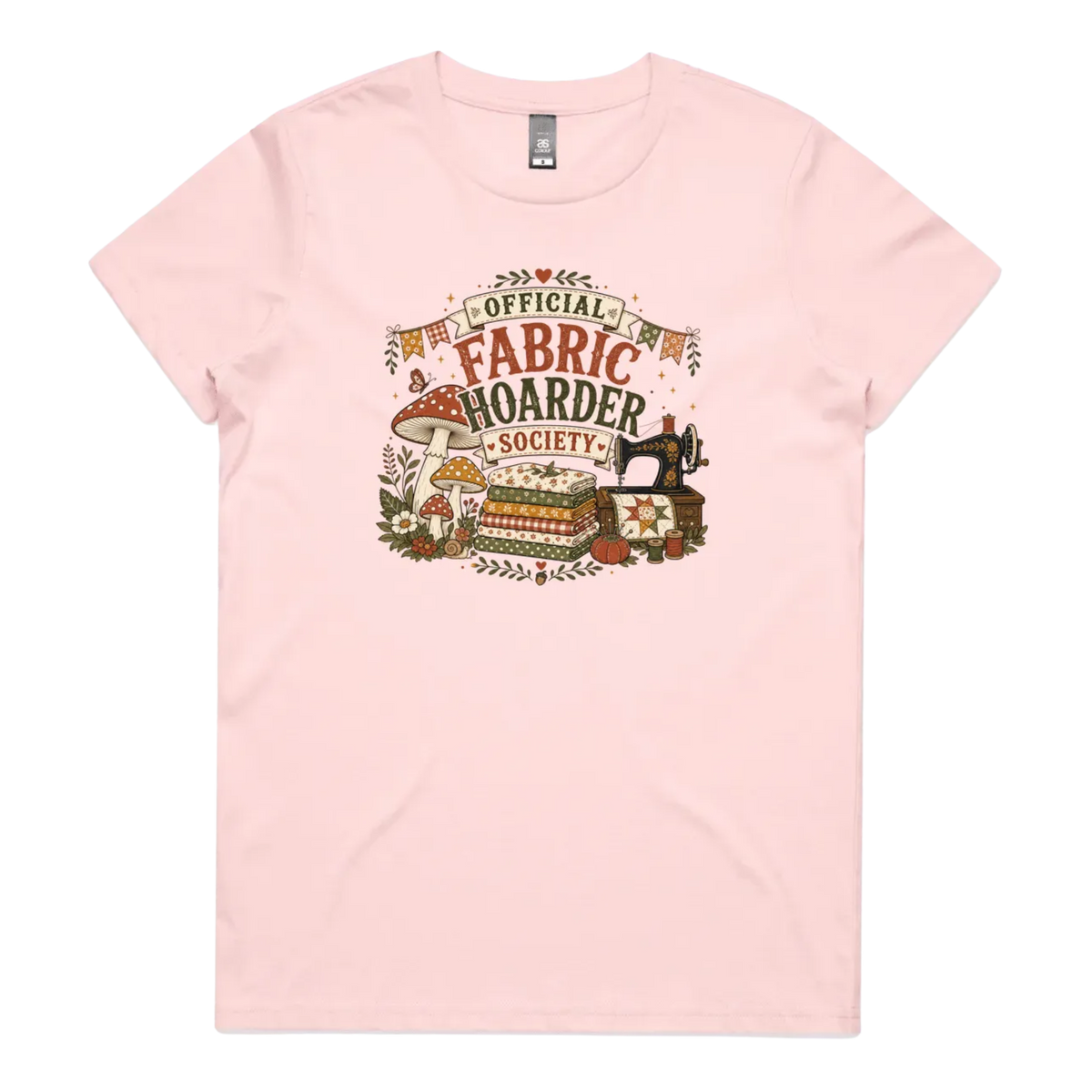 A pale pink crewneck short-sleeved t-shirt with the words 'Official Fabric Hoarder Society' above an illustration of a stack of fabric, a sewing machine and a group of muchrooms, flowers and a snail.