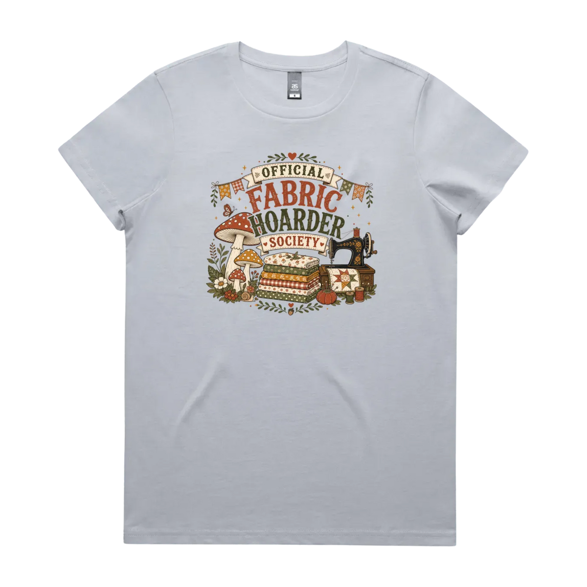 A pale powder blue crewneck short-sleeved t-shirt with the words 'Official Fabric Hoarder Society' above an illustration of a stack of fabric, a sewing machine and a group of muchrooms, flowers and a snail.