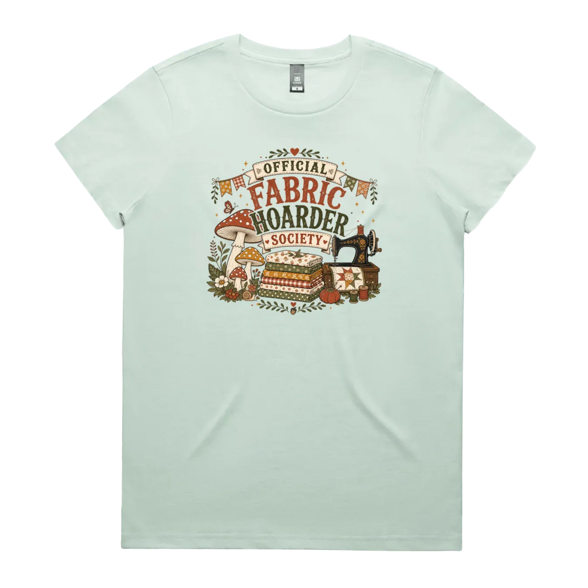 A pale seafoam green crewneck short-sleeved t-shirt with the words 'Official Fabric Hoarder Society' above an illustration of a stack of fabric, a sewing machine and a group of muchrooms, flowers and a snail.