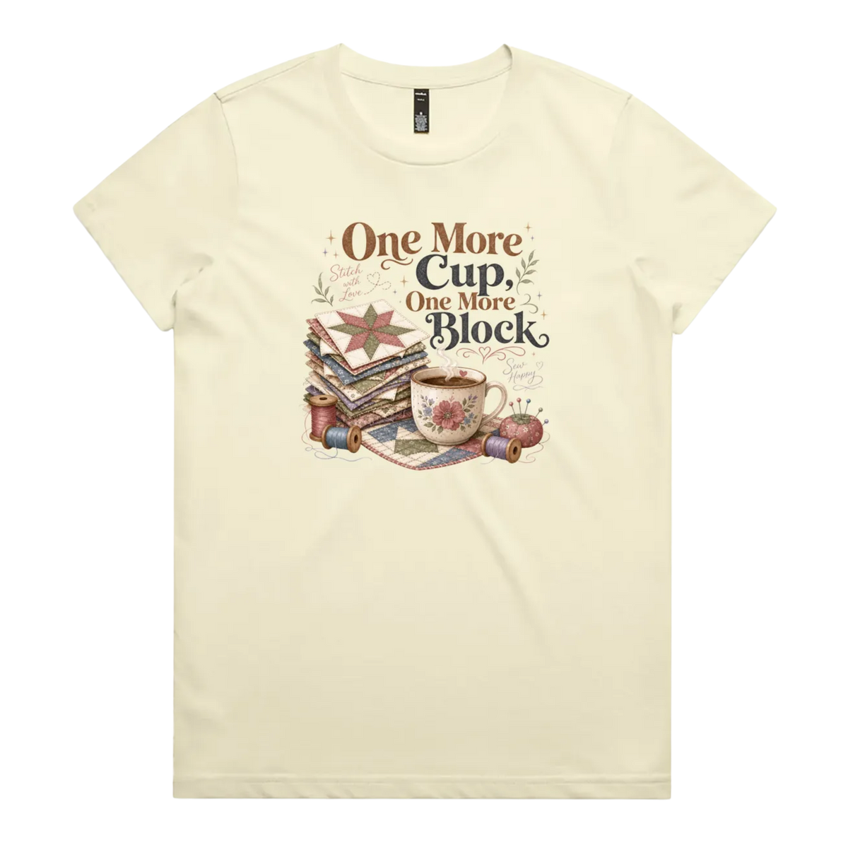 A pale butter yellow short-sleeve crewneck t-shirt featuring a vintage-style graphic of stacked quilt blocks, a coffee cup, and thread spools with the text 'One More Cup, One More Block' in brown and black lettering.