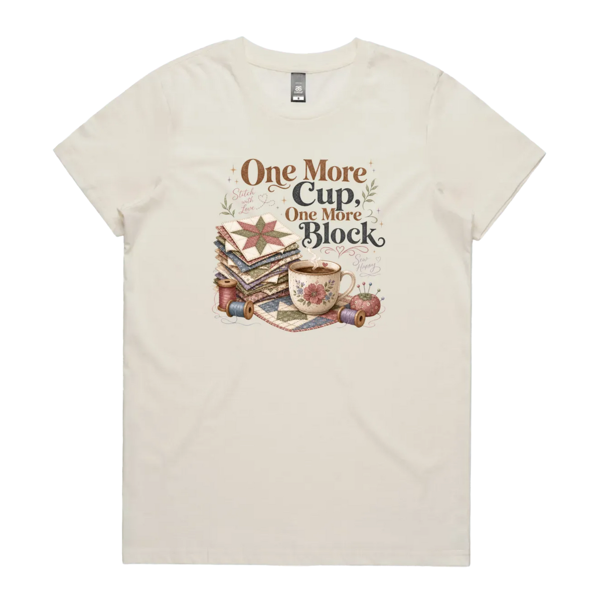 A pale cream short-sleeve crewneck t-shirt featuring a vintage-style graphic of stacked quilt blocks, a coffee cup, and thread spools with the text 'One More Cup, One More Block' in brown and black lettering.