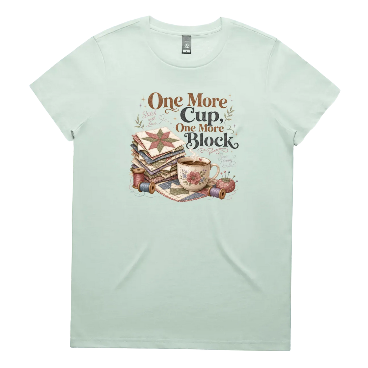 A pale seafoam green short-sleeve crewneck t-shirt featuring a vintage-style graphic of stacked quilt blocks, a coffee cup, and thread spools with the text 'One More Cup, One More Block' in brown and black lettering.