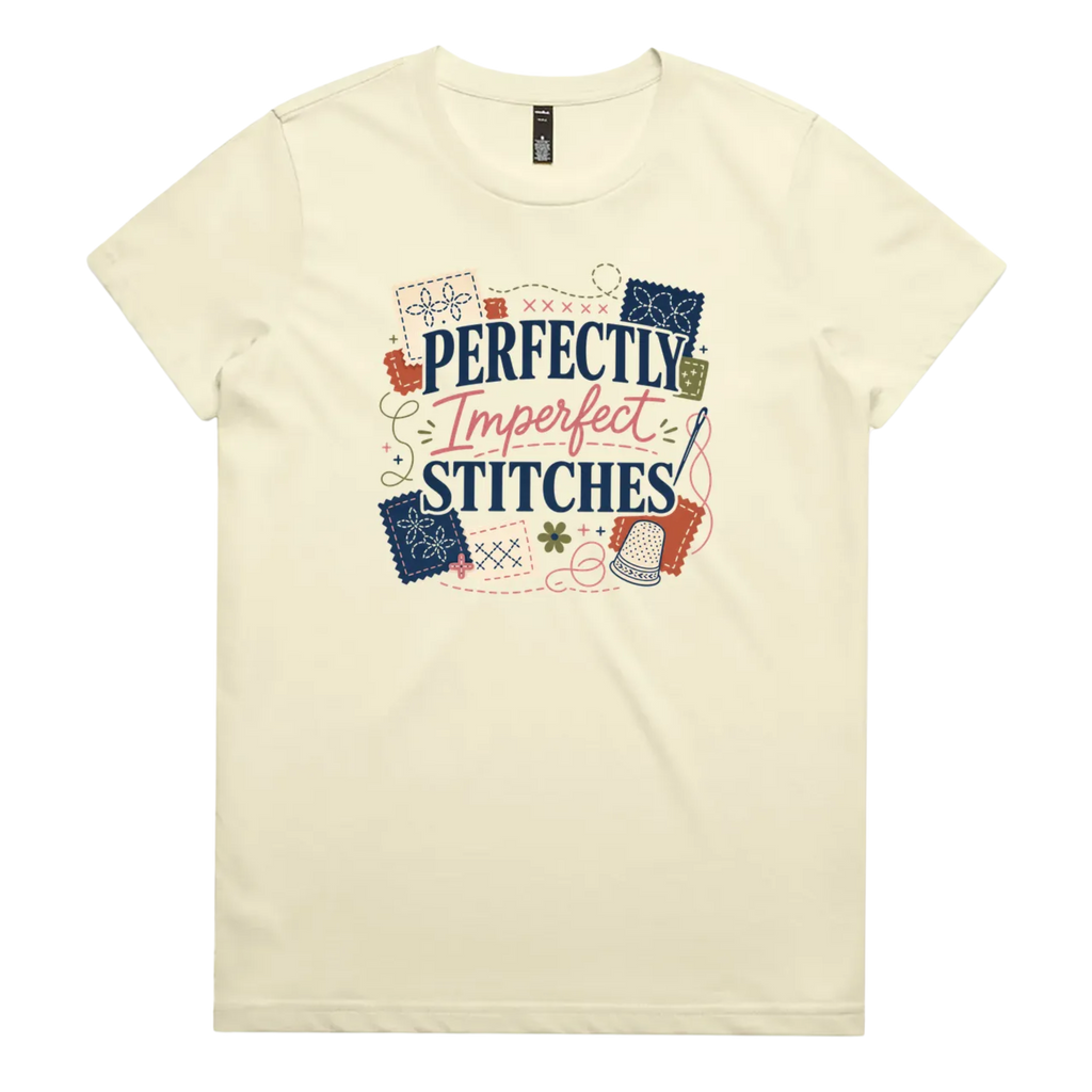 A pale butter yellow short-sleeve crewneck t-shirt featuring a colorful graphic print on the front with the text 'Perfectly Imperfect Stitches' surrounded by sashiko-themed illustrations.