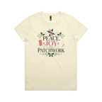 A pale butter yellow short-sleeve crewneck t-shirt with a central graphic print that reads 'Peace, Joy & Patchwork' in dark lettering, decorated with a pink bow, quilt block, spool of thread, needle, and floral elements.