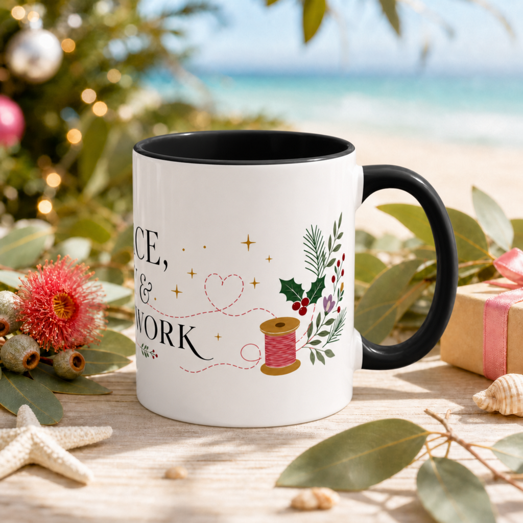 The right side of a white ceramic mug with a black handle and interior, decorated with a thread spool, stitch lines, holly, berries and flowers. The text ‘Peace, Joy & Patchwork' is partially visible. The mug is styled on a wooden surface with eucalyptus leaves, a starfish, a pink flower, and a blurred beach and Christmas tree background.
