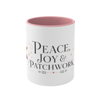 The front of a white ceramic mug with a pink interior and rim, showing the words ‘Peace, Joy & Patchwork'. The text is styled in black fonts with small heart and leaf accents.