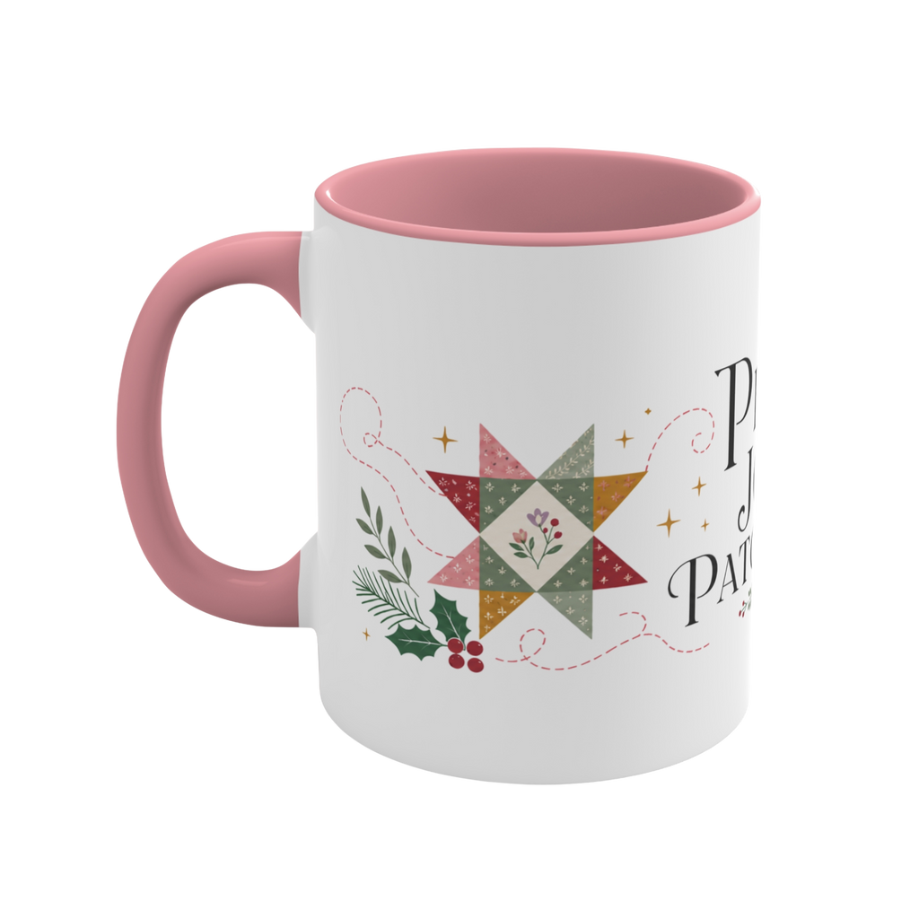 The left side of a white ceramic mug with a pink handle and interior, decorated with a quilt block, stitch lines and holly. The text ‘Peace, Joy & Patchwork' is partially visible.