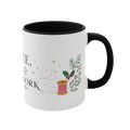 The right side of a white ceramic mug with a black handle and interior, decorated with a thread spool, stitch lines, holly, berries and flowers. The text ‘Peace, Joy & Patchwork' is partially visible.