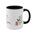 The right side of a white ceramic mug with a black handle and interior, decorated with a thread spool, stitch lines, holly, berries and flowers. The text ‘Peace, Joy & Patchwork' is partially visible.