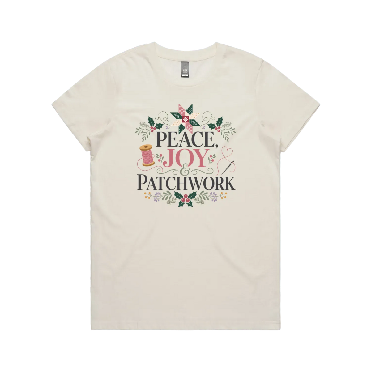 An off-white short-sleeve crewneck t-shirt with a central graphic print that reads 'Peace, Joy & Patchwork' in dark lettering, decorated with a pink bow, quilt block, spool of thread, needle, and floral elements.