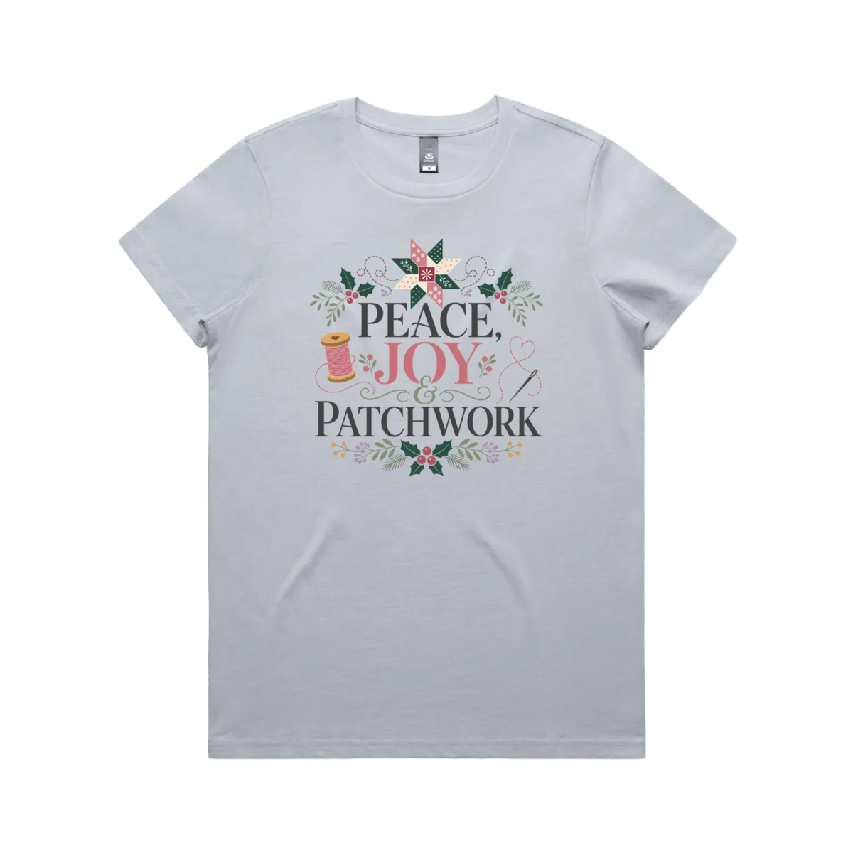 A powder blue short-sleeve crewneck t-shirt with a central graphic print that reads 'Peace, Joy & Patchwork' in dark lettering, decorated with a pink bow, quilt block, spool of thread, needle, and floral elements.