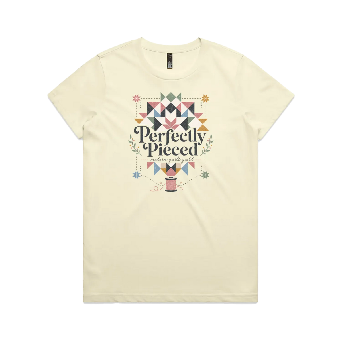 A pale butter yellow graphic short-sleeve t-shirt with the words 'Perfectly Pieced Modern Quilt Guild' cutting through a large patchwork star.