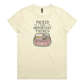 A pale butter yellow short-sleeve crewneck t-shirt featuring a graphic print on the front with the text 'PACKED THE IMPORTANT THINGS' above an illustration of a pink bag filled with quilting supplies.