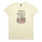 A pale butter yellow short-sleeve crewneck t-shirt featuring a graphic print on the front with the text 'PACKED THE IMPORTANT THINGS' above an illustration of a pink bag filled with quilting supplies.