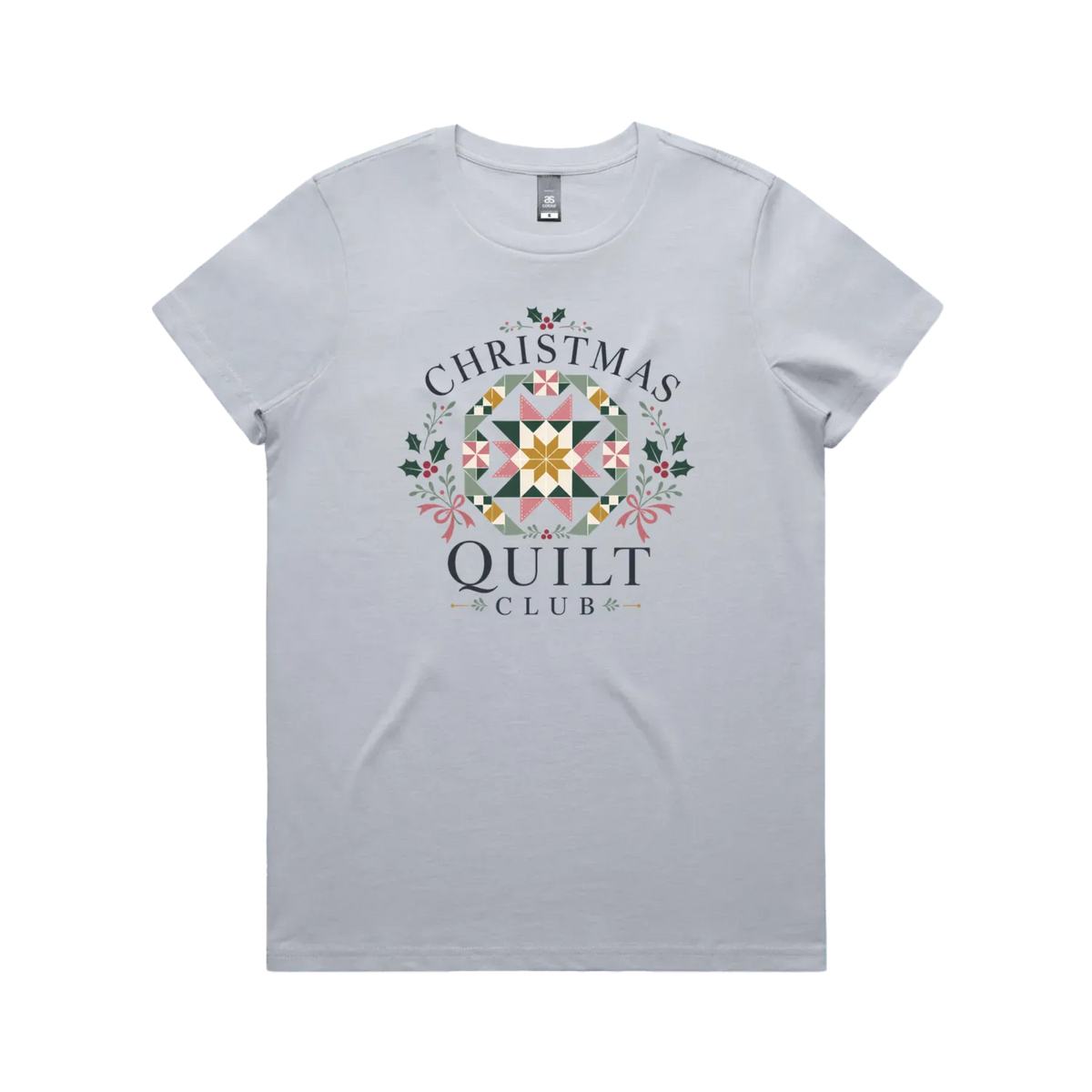A powder blue short-sleeve crewneck t-shirt featuring a 'Christmas Quilt Club' graphic on the front. The graphic includes a colorful geometric quilt pattern in the center, surrounded by green holly leaves and pink bows, with the words 'CHRISTMAS QUILT CLUB' printed in dark gray.