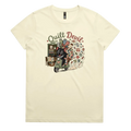 A pale butter yellow short-sleeve crewneck t-shirt featuring a colorful graphic print of a Tasmanian Devil riding a green scooter, surrounded by quilts, fabric and quilting tools with the text 'Quilt Devil'.