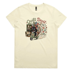 A pale butter yellow short-sleeve crewneck t-shirt featuring a colorful graphic print of a Tasmanian Devil riding a green scooter, surrounded by quilts, fabric and quilting tools with the text 'Quilt Devil'.