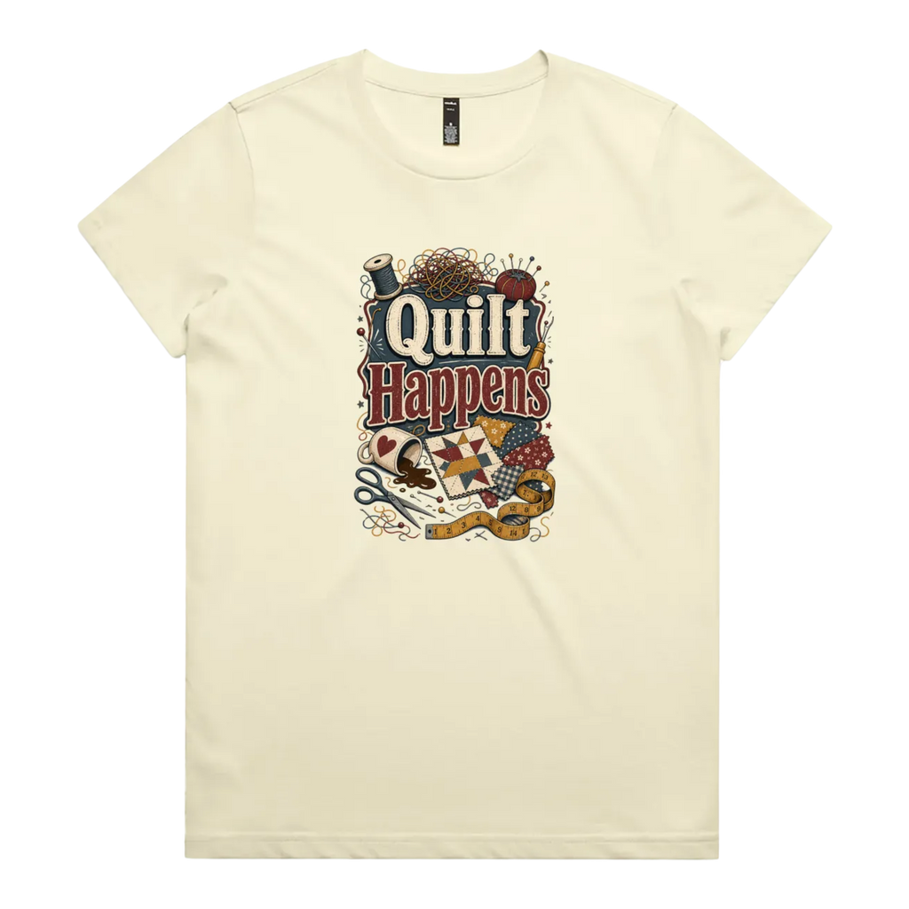 A pale butter yellow short-sleeve crewneck t-shirt featuring a colorful graphic print on the front with the text 'Quilt Happens' surrounded by quilting tools and fabrics.