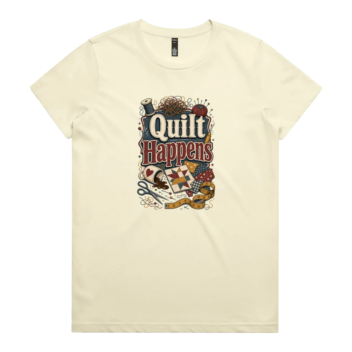 A pale butter yellow short-sleeve crewneck t-shirt featuring a colorful graphic print on the front with the text 'Quilt Happens' surrounded by quilting tools and fabrics.