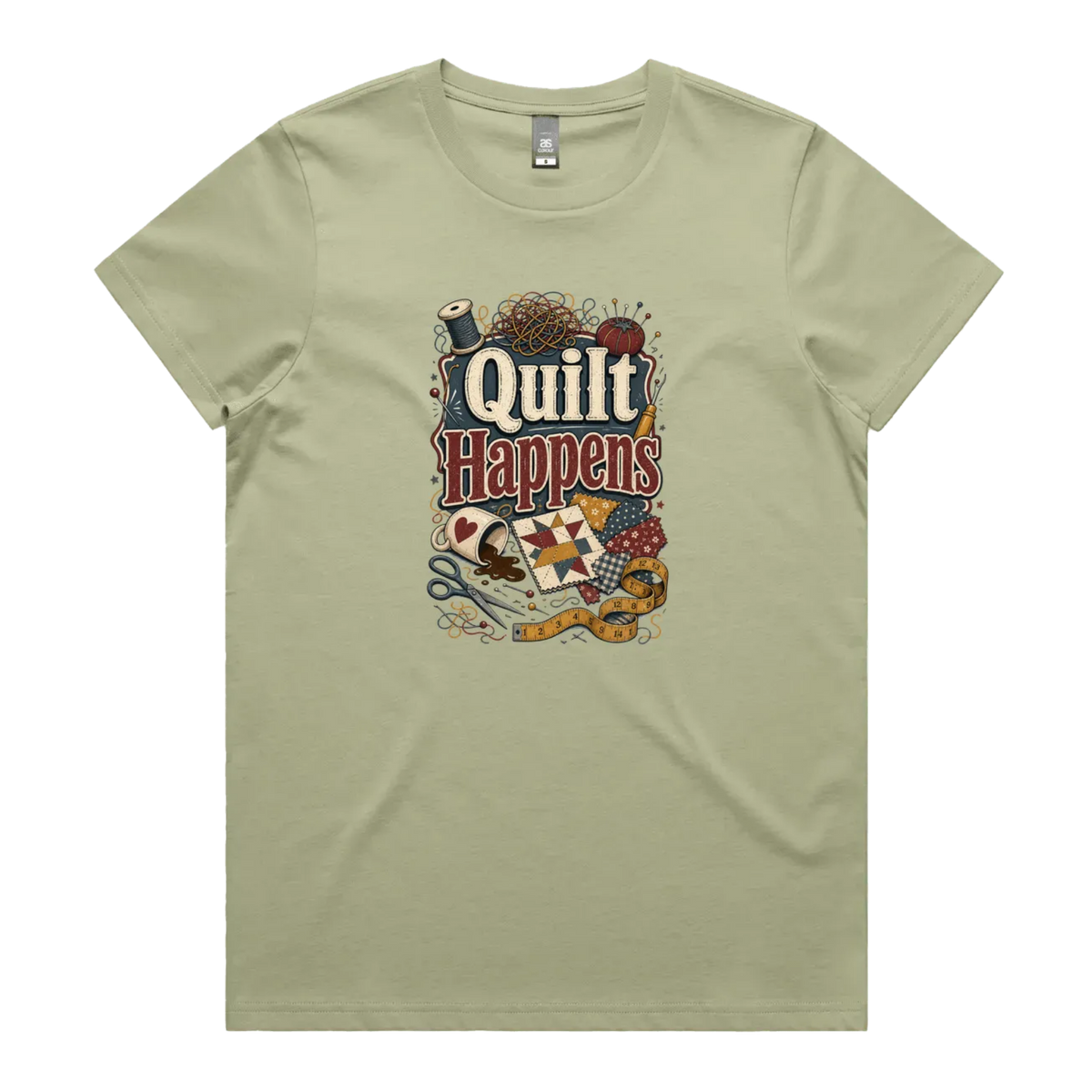 A pale pistachio green short-sleeve crewneck t-shirt featuring a colorful graphic print on the front with the text 'Quilt Happens' surrounded by quilting tools and fabrics.