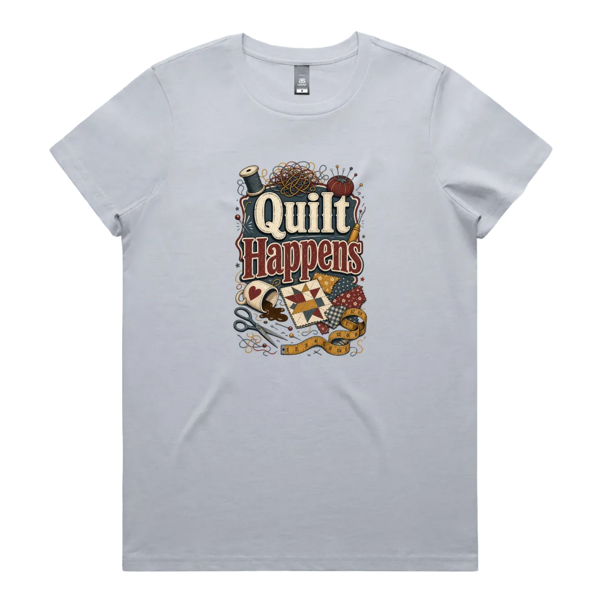 A pale powder blue short-sleeve crewneck t-shirt featuring a colorful graphic print on the front with the text 'Quilt Happens' surrounded by quilting tools and fabrics.