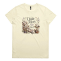 A pale butter yellow short-sleeve crewneck t-shirt featuring a vintage-style graphic on the front with the text 'Quilt More, Sip Slowly' surrounding an illustration of a quilted armchair, floral details, and sewing tools.