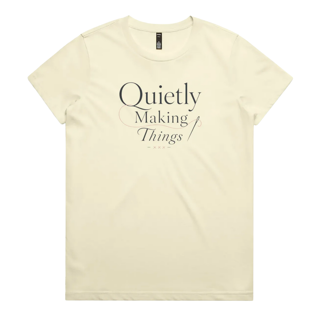 A pale butter yellow short-sleeve crewneck t-shirt with a dark gray text graphic on the front reading 'Quietly Making Things' with needle and thread accents.