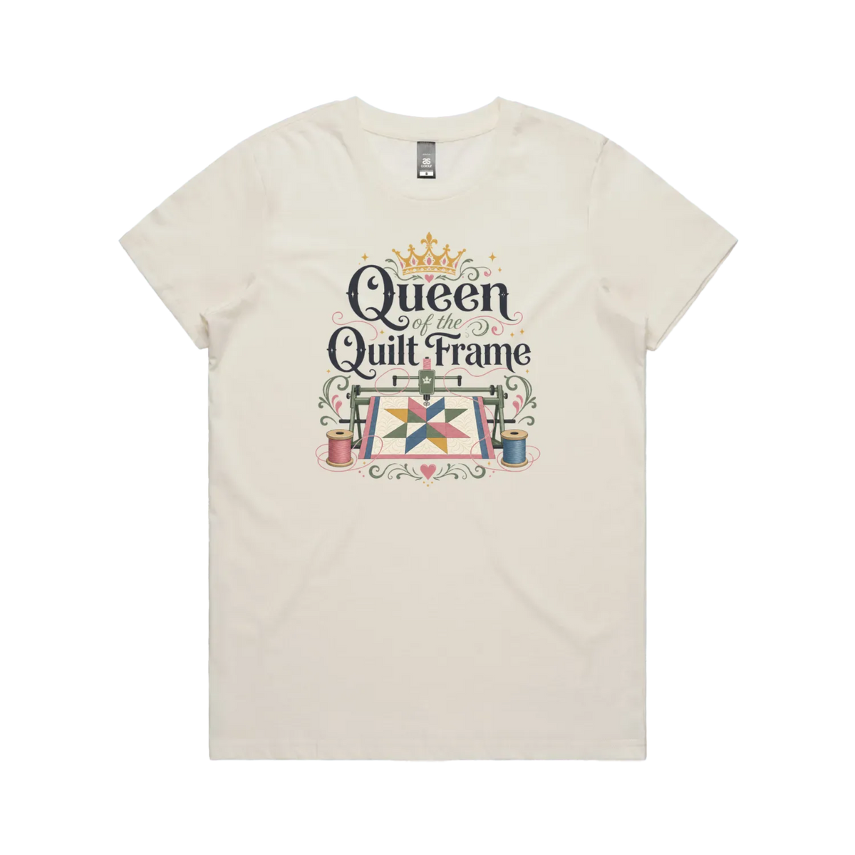 An off-white short-sleeve t-shirt with a graphic print on the front that reads 'Queen of the Quilt Frame' in black script, decorated with a gold crown, a quilt design, and spools of thread.