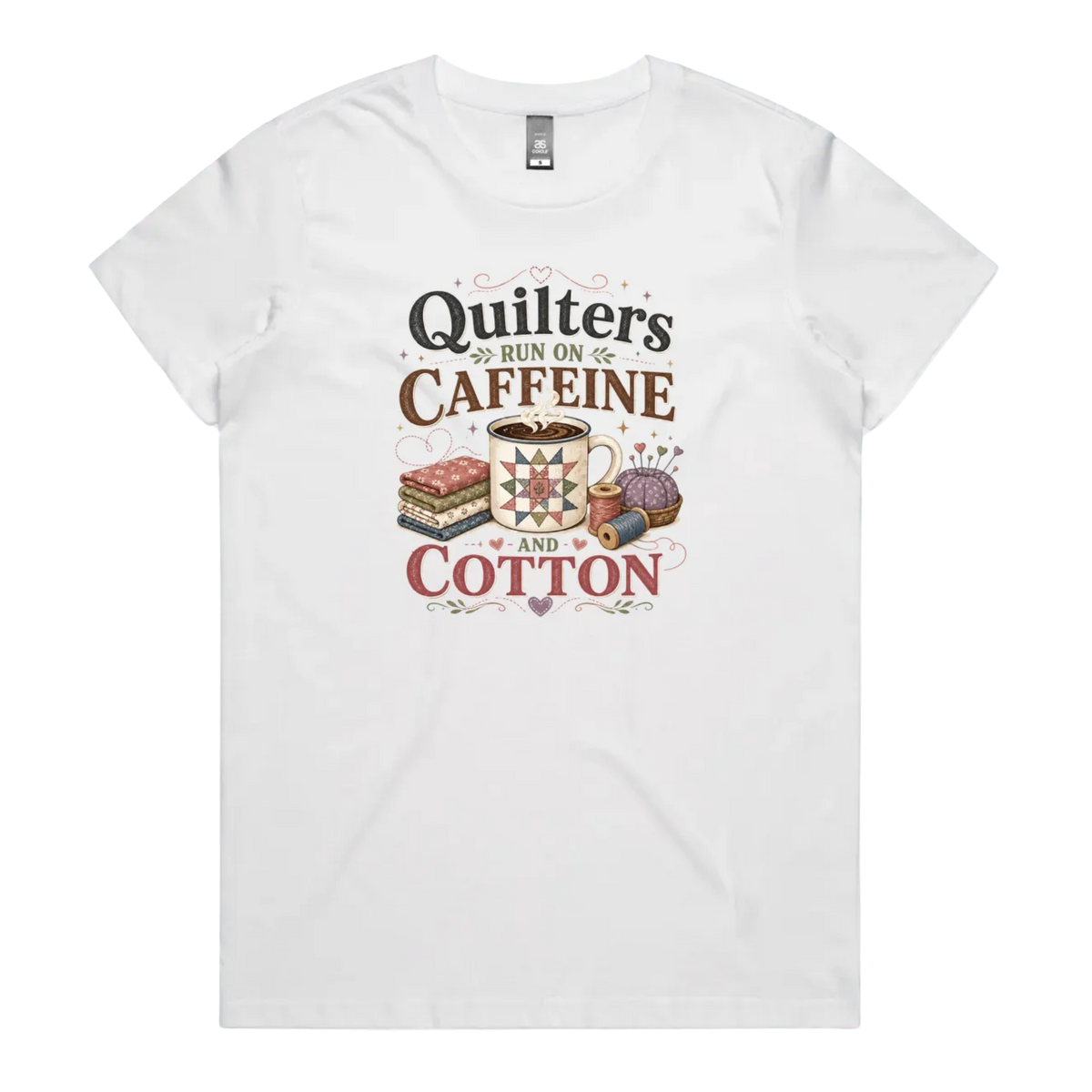 A white short-sleeve crewneck t-shirt featuring a retro-style graphic print on the front. The graphic reads 'Quilters Run on Caffeine and Cotton' in stylized fonts, accompanied by illustrations of a fabric stack, a mug of coffee, a pincushion, and a spool of thread.