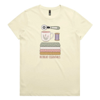 A light butter yellow short-sleeve crewneck t-shirt featuring a graphic of sewing and crafting essentials (a rotary cutter, mug, fabric stack, spool of thread) with the text 'RETREAT ESSENTIALS' printed below.