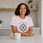 A woman with dark hair sitting at a kitchen bench wearing a pale mauve graphic t-shirt with the words 'Scrappy but Sophisticated' above a large star quilt block.