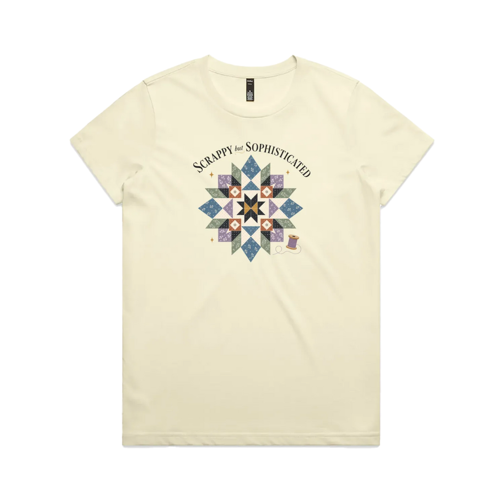 A pale butter yellow short-sleeve crewneck tshirt with the words 'Scrappy but Sophisticated' above a large star quilt block with a purple thread spool on the bottom right.