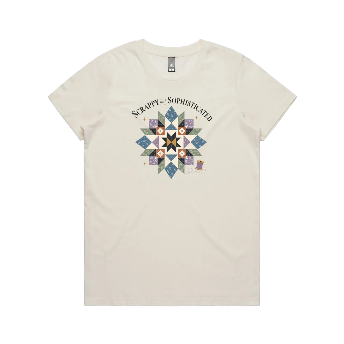 A pale cream short-sleeve crewneck tshirt with the words 'Scrappy but Sophisticated' above a large star quilt block with a purple thread spool on the bottom right.